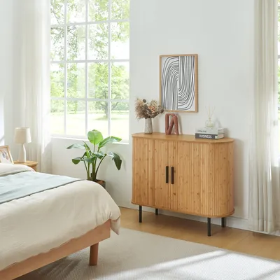 A bedroom scene with a bed, a plant, and a wooden cabinet.