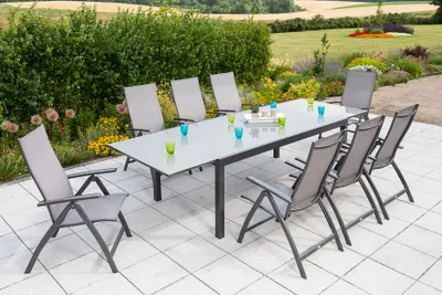 A garden dining set with a table and chairs on a patio, surrounded by greenery and flowers.