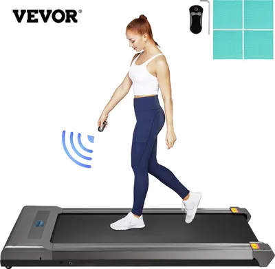 A woman is walking on a compact treadmill under a desk, holding a remote control. There are also some accessories shown in the top right corner.