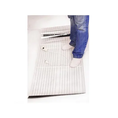 A person wearing blue jeans and white socks stands on a heating mat.