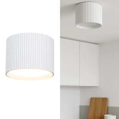A white cylindrical ceiling lamp with vertical ridges, shown in isolation and installed in a kitchen.