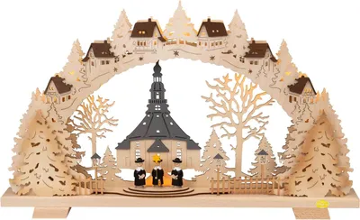 Ein Schwibbogen aus dem Erzgebirge zeigt eine Szene mit der Seiffener Kirche umgeben von Bäumen und drei Kurrendefiguren während im Hintergrund oberhalb der Kirche Häuser zu sehen sind
