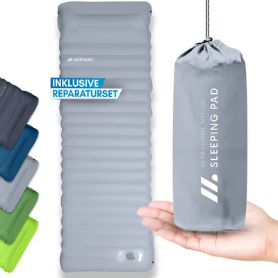A hand holding a grey sleeping pad bag next to an unrolled grey sleeping pad, with other sleeping pads in different colors stacked on the left.