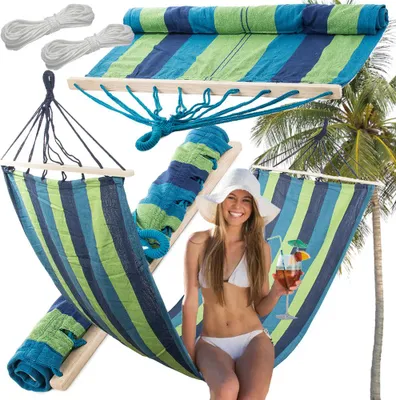 A woman in a bikini relaxing in a hammock with a drink, with a palm tree in the background.