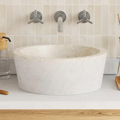 A close-up view of a cream-colored marble sink with a faucet and soap dispenser in the background.