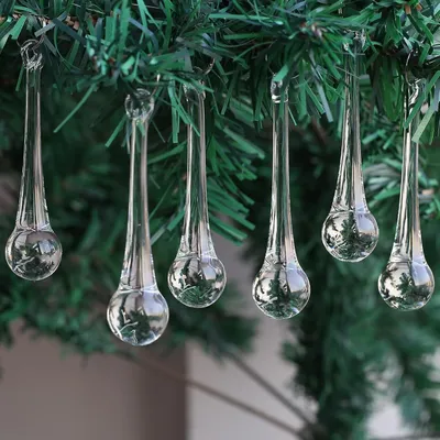 Clear glass icicle ornaments hanging from a green artificial Christmas tree.