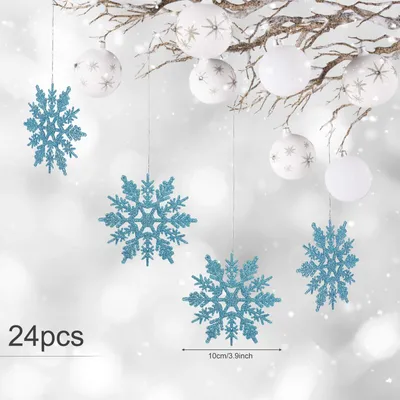 Hanging Christmas ornaments, including blue glitter snowflakes and white baubles with star patterns, against a blurred snowy background.