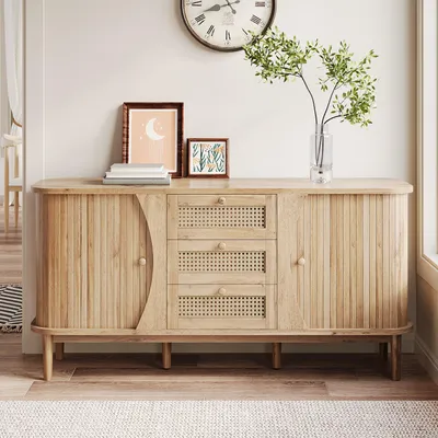 A light wood sideboard with cane accents, decorated with framed art and a vase of greenery, displayed in a well-lit room.