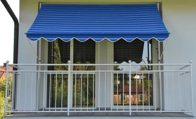 A blue and white striped awning is installed above a balcony with a white railing.