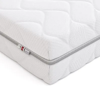 A close-up, angled view of a white mattress with a quilted pattern and a gray trim along the edge. There are small tags attached to the trim.