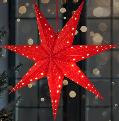 A red star-shaped lantern with small yellow lights is hanging in front of a window with blurred lights in the background.