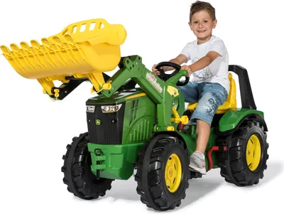 A young boy is riding a green and yellow toy tractor with a front loader.