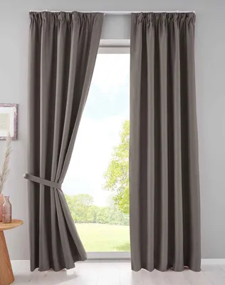 A pair of taupe blackout curtains are shown hanging in front of a window with a view of trees and grass.