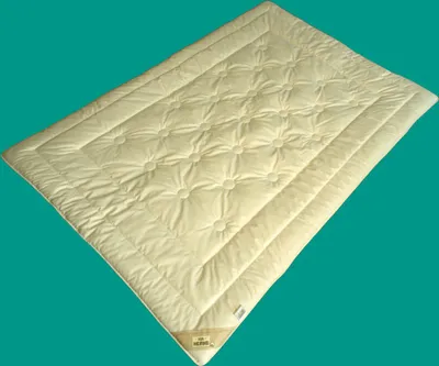 A cream-colored quilted blanket or comforter is shown diagonally against a teal background.