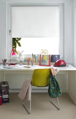 A desk with a roller blind, a chair, and various school supplies.