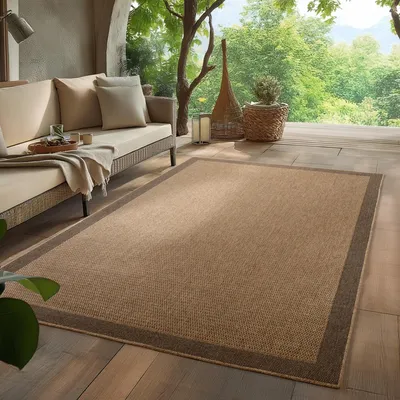 An outdoor living space with a sofa and a rug on a wooden deck, surrounded by greenery.