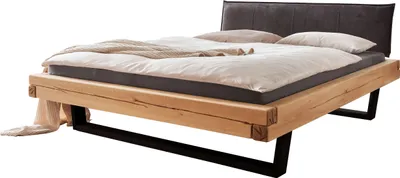 A bed with a wooden frame and a dark headboard, made with linens and blankets.