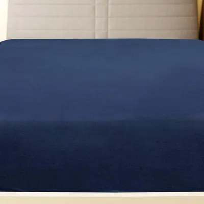 A close-up view of a navy blue fitted sheet on a bed, with a light gray headboard visible in the background.
