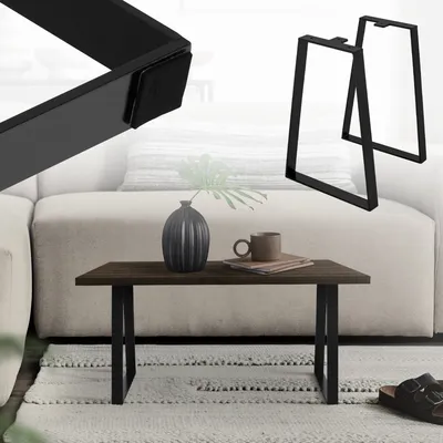 A coffee table with black trapezoidal legs, a dark wood top, a vase, and a mug on a rug in front of a sofa.