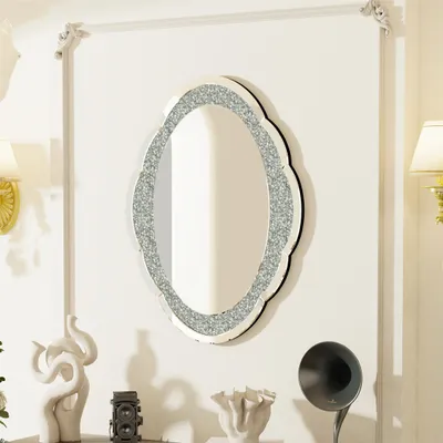 A decorative oval mirror with a glittery border hangs on a white wall, surrounded by decorative objects and a lamp.