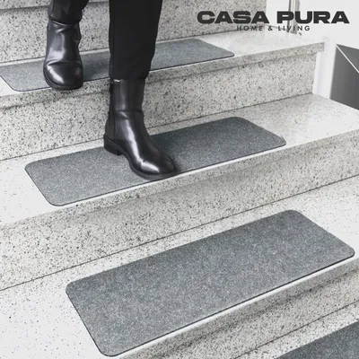 A person wearing black boots walks down a set of stairs covered with gray stair mats.