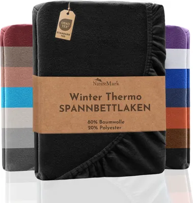 A folded black fitted sheet is displayed prominently, with other colored sheets stacked behind it. A brown paper band wraps around the middle of the black sheet, featuring product information and a brand logo.