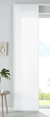 A white panel curtain hanging in front of a large window with a view of greenery outside. A small side table with a plant and a decorative object is visible to the left.