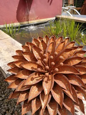 A rusted metal flower sculpture sits in front of a pond with a small waterfall.