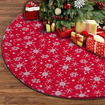 A Christmas tree skirt with a snowflake pattern is laid out on a wooden floor, with wrapped presents and a Santa sack placed around the base of a Christmas tree.