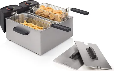 A stainless steel double deep fryer with two baskets, one filled with french fries and the other with chicken nuggets. Two lids are placed in front of the fryer.