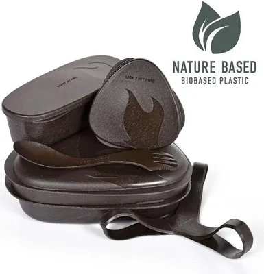 A set of brown bio-based plastic lunch containers and utensils, stacked and arranged on a white background. Text and a leaf logo are visible in the upper right corner.