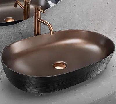 A close-up shot of a modern oval countertop sink with a copper faucet.