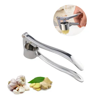 A stainless steel garlic press with a white handle, shown on a white background. There are also some garlic bulbs and ginger slices in the lower left corner. A small inset image shows the garlic press in use.