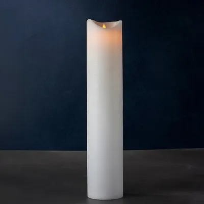 A tall, white LED candle with a flickering flame sits on a dark surface against a dark blue background.