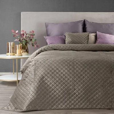 A neatly made bed with a beige quilted bedspread and purple pillows.