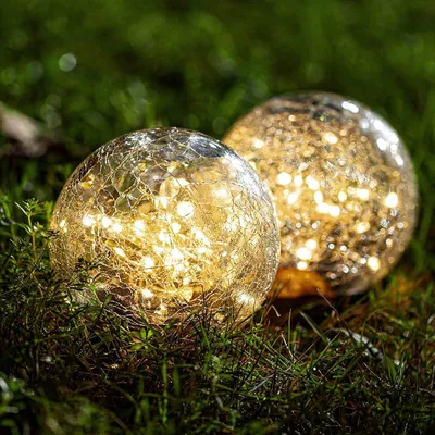 Two solar-powered glass orbs with embedded LED lights sit on green grass.