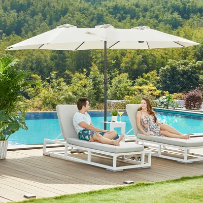 A couple relaxing on lounge chairs by a pool under a large umbrella.