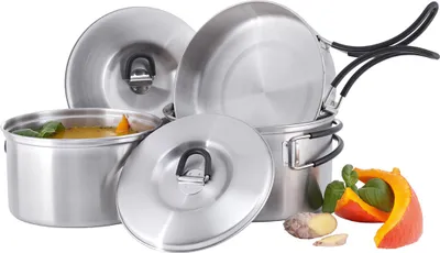 A set of camping cookware, including pots and pans, arranged on a white background with some ginger and pumpkin slices.