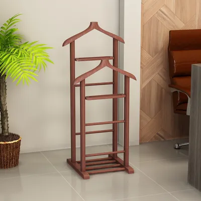A wooden valet stand is shown in a room with a plant and a chair in the background.