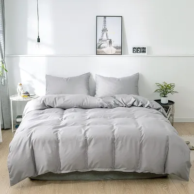A neatly made bed with gray bedding in a room with white walls.