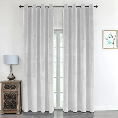 A pair of white velvet curtains hangs in front of a window, with a bedside table and lamp to the left and a framed picture on the wall to the right.