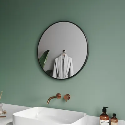 A modern bathroom with a round black mirror, a white sink, and copper faucets.