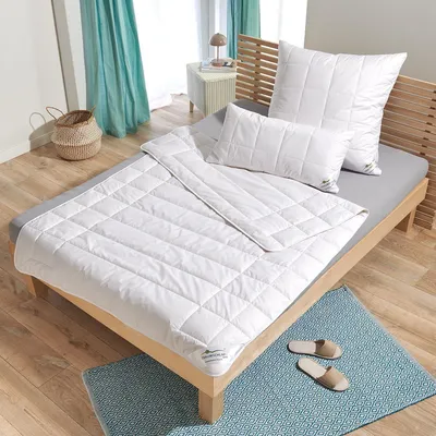 A neatly made bed with white bedding and pillows, set in a bedroom with wooden flooring and teal curtains.