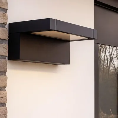 A black LED outdoor wall light mounted on a white wall next to a brick wall and a window.