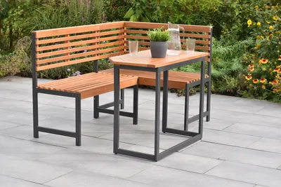 An outdoor seating set with a corner bench and a table on a patio, surrounded by plants.