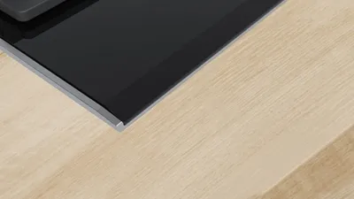 Close-up of a black glass stovetop with a silver trim, placed on a light wood surface.