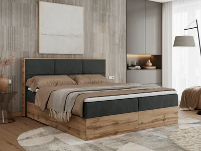 A bedroom scene featuring a large boxspring bed with a wooden frame and upholstered headboard, dressed with bedding and throws. The room also includes a wardrobe and a floor lamp.