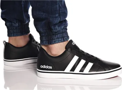A person wearing black Adidas VS Pace sneakers and blue jeans.