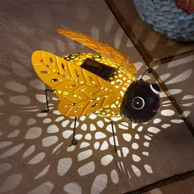 A solar-powered decorative bee lantern casting patterned light on a stone surface.