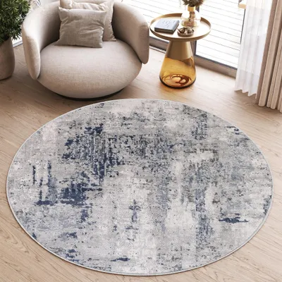 A round rug with a distressed pattern is placed on a wooden floor in a living room setting, next to a modern armchair and a side table.